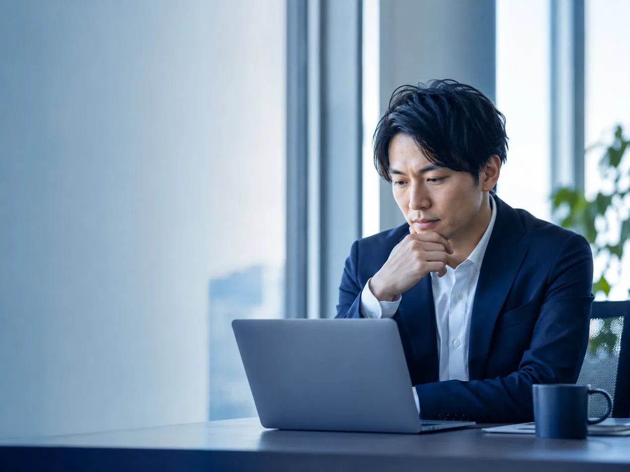 ノートパソコンの前で考え込むビジネスパーソン